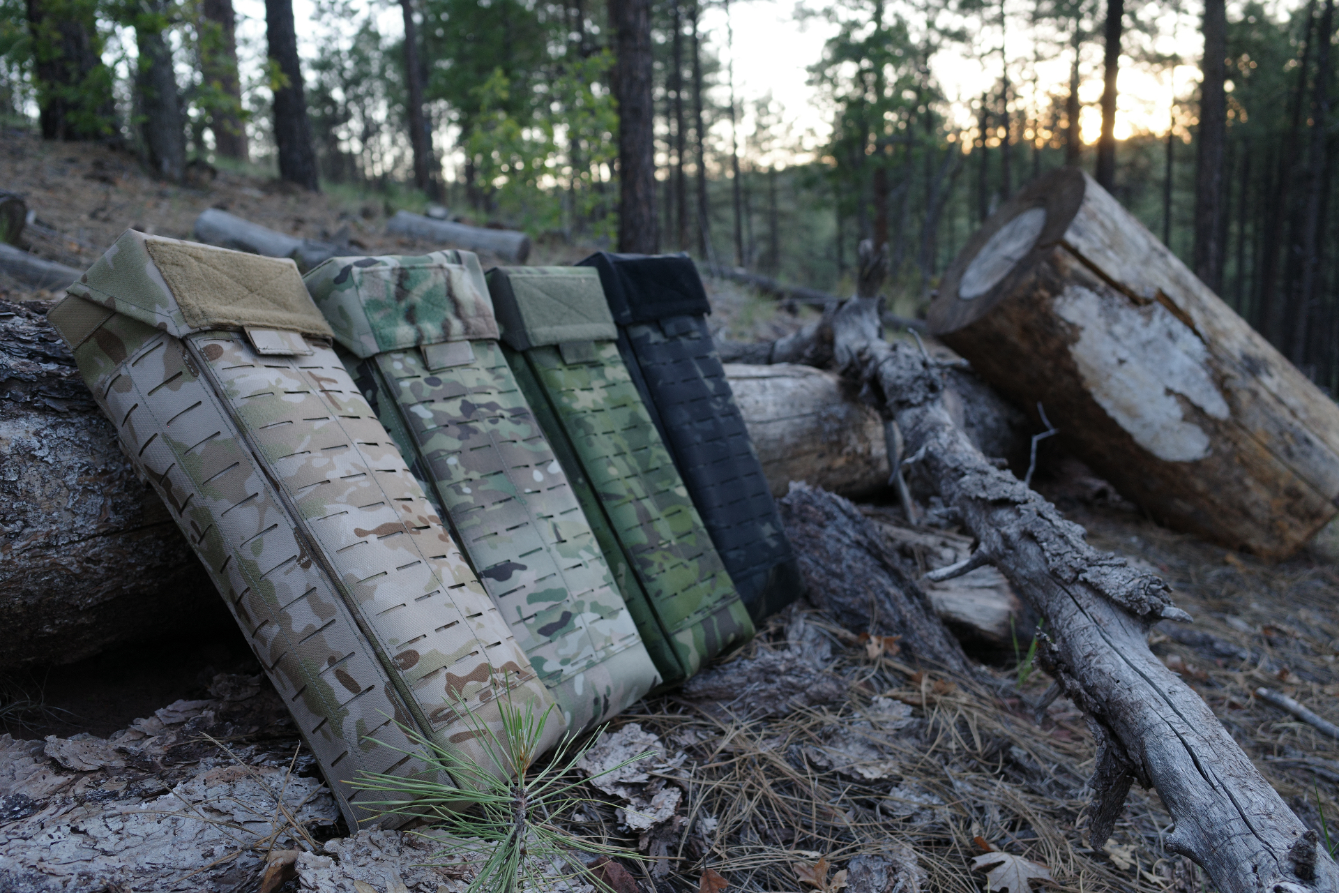Four Fieldcraft glove bags in MultiCam Arid, MultiCam, Ranger Green, and Black lined up on a fallen log at sunset